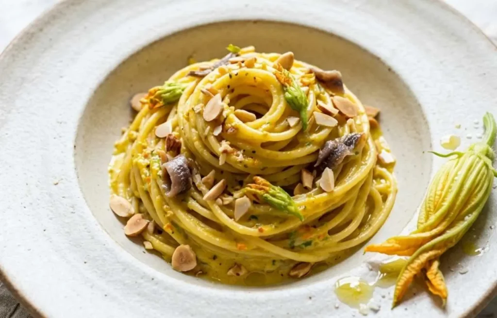 Spaghetti cremosi conditi con pesto di fiori di zucca a crudo, mandorle e alici sott'olio