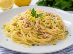 Piatto di spaghetti con tonno e limone servito su piatto bianco, guarnito con scorza di limone grattugiata e prezzemolo fresco.