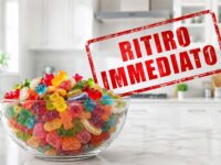 Grande ciotola di vetro con caramelle gommose assortite in primo piano in una cucina bianca moderna e luminosa con timbro rosso Ritiro Immediato