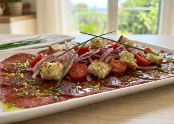 Bresaola stesa su un piatto piano marinata con limone e arancia, coperta da un'insalata croccante di finocchi rossi affettati finissimi, pomodorini ciliegino a metà e crostini di pane tostato al timo.