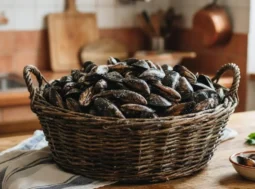 Cesta in vimini piena di cozze fresche su un tavolo di legno in cucina, pronta per la pulizia e la cottura.