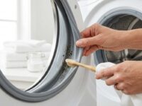 Mano che pulisce la guarnizione in gomma della lavatrice con uno spazzolino e pasta di bicarbonato