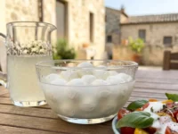 Una ciotola di vetro con mozzarelle nel loro liquido e una salsa bianca cremosa versata su un'insalata