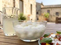 Una ciotola di vetro con mozzarelle nel loro liquido e una salsa bianca cremosa versata su un'insalata