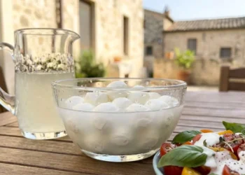 Una ciotola di vetro con mozzarelle nel loro liquido e una salsa bianca cremosa versata su un'insalata