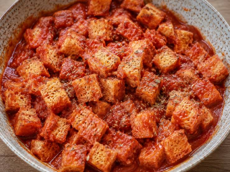 Trasferite i cubetti di pane direttamente nella ciotola con il condimento al pomodoro. Mescolate con cura e delicatezza, facendo in modo che ogni cubetto assorba uniformemente il pomodoro senza però inzupparsi eccessivamente. Foderate una teglia capiente con della carta da forno. Distribuite i cubetti di pane conditi sulla teglia in un solo strato, evitando di sovrapporli, così da garantire una doratura e una croccantezza uniformi