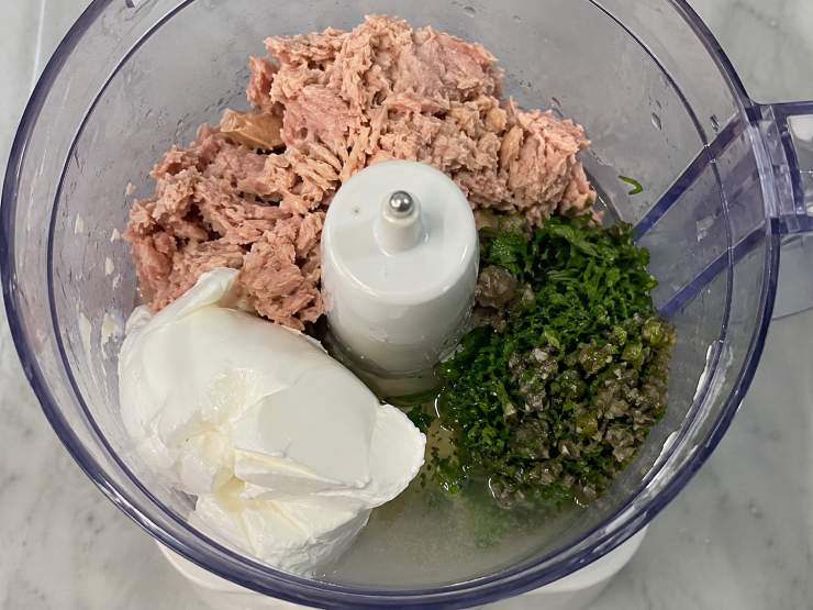 Unite all’interno di un mixer o direttamente in una ciotola capiente il tonno ben sgocciolato, il formaggio spalmabile scelto, il trito di capperi e prezzemolo e un mestolino di acqua di cottura della pasta, fondamentale per garantire la giusta cremosità. Frullate o mescolate energicamente il tutto fino a ottenere una crema liscia, vellutata e omogenea.