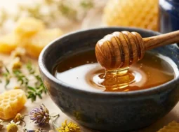 Miele sulla pelle e rimedi naturali anti-age Miele millefiori biologico in una ciotola con spargimiele e fiori di camomilla per la cura naturale della pelle
