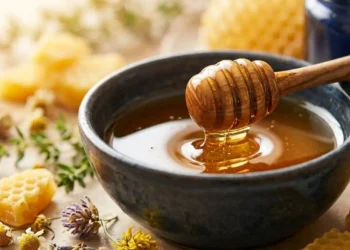 Miele sulla pelle e rimedi naturali anti-age Miele millefiori biologico in una ciotola con spargimiele e fiori di camomilla per la cura naturale della pelle