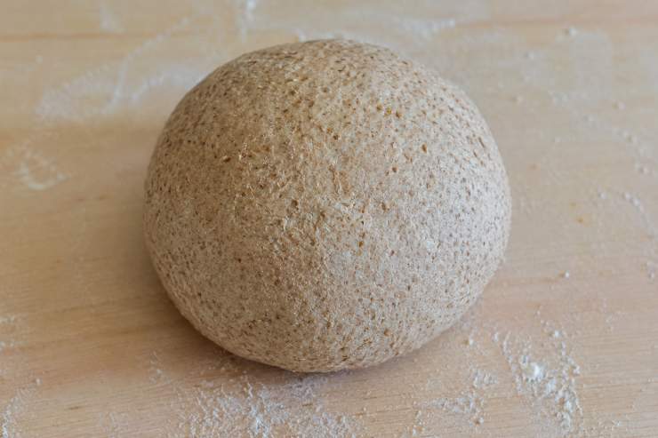 In una ciotola capiente versate la farina integrale, il sale ed il bicarbonato. Unite l’olio extravergine d’oliva ed iniziate a incorporare l’acqua tiepida poco alla volta, impastando prima con una forchetta e poi a mano. Trasferite l’impasto su una spianatoia e lavoratelo energicamente per circa 5-10 minuti fino ad ottenere un panetto liscio, morbido ed elastico. Avvolgetelo nella pellicola trasparente e lasciatelo riposare a temperatura ambiente per 30 minuti.