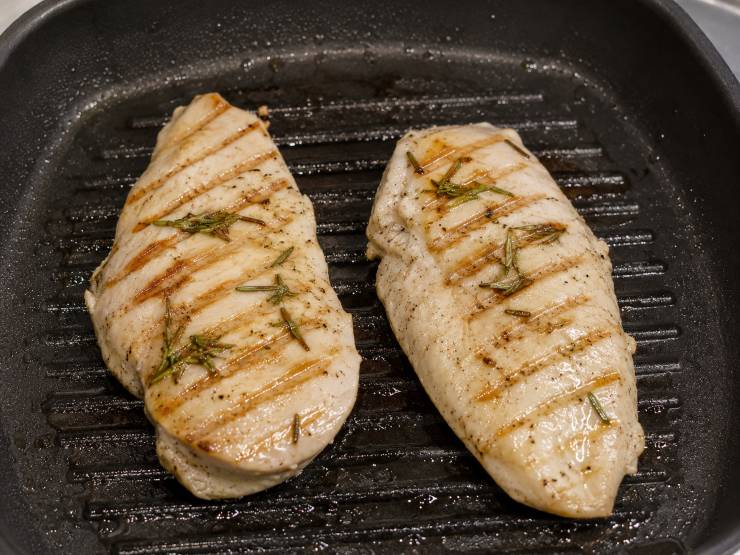 Scaldate molto bene una piastra o una griglia in ghisa: sgocciolate il pollo dalla marinatura e cuocetelo a fiamma media per circa 4 minuti per lato a seconda dallo spessore. Una volta cotto, trasferite il pollo su un tagliere e lasciatelo raffreddare completamente a temperatura ambiente. Questo permetterà alle fibre della carne di rilassarsi, garantendo una morbidezza unica.