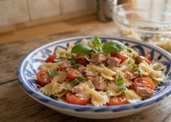 Piatto di farfalle fredde al tonno e pomodorini guarnito con basilico fresco, pronto per essere servito.