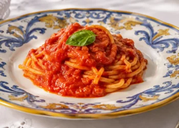 Nido di spaghetti alla Devozione di Peppe Guida lucidi e cremosi conditi con sugo di pomodoro San Marzano e foglia di basilico fresco in un piatto bianco.