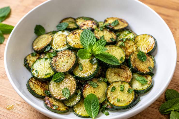 A questo punto potete preparare il condimento unendo in una ciotola l’aceto di vino bianco, un pizzico di sale, due spicchi di aglio tritati finemente, tante foglie di menta fresca spezzettate con le mani e olio extra vergine di oliva. Condite le zucchine in una ciotola con questa marinatura e lasciate riposare almeno due ore in frigo, coprendo con della pellicola per alimenti