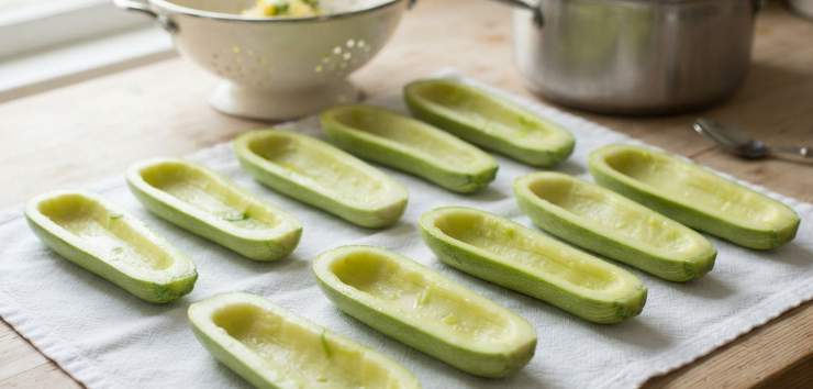 Innanzitutto, lavate accuratamente le zucchine, spuntatele e tagliatele a metà nel senso della lunghezza. Svuotate delicatamente la polpa interna con l’aiuto di un cucchiaino o di uno scavino, facendo attenzione a non rompere il guscio esterno che farà da contenitore. Sbollentate i gusci di zucchina in acqua bollente salata per circa 3-4 minuti, quindi scolateli e fateli raffreddare capovolti su un canovaccio pulito. Tritate finemente la polpa di zucchina estratta. In una ciotola capiente, bagnate il pane raffermo con il latte fino a farlo ammorbidire completamente, poi strizzatelo bene.