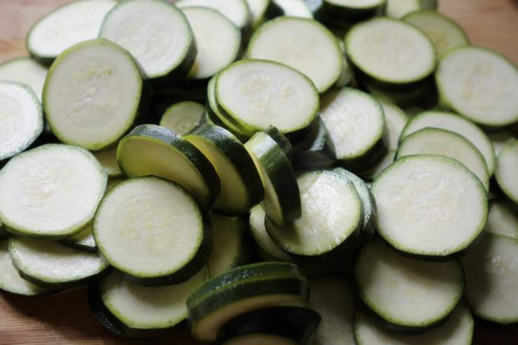 Come prima cosa lavate le zucchine, asciugatele con cura, togliete le estremità e tagliatele a rondelle di 3 millimetri di spessore. Cospargetele di sale e lasciatele riposare in uno scolapasta in modo che perdano parte dell’acqua di vegetazione. Dopo mezz’ora circa risciacquatele bene e asciugatele con un canovaccio ben pulito o con carta assorbente da cucina.