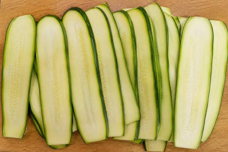 Lavate accuratamente le zucchine sotto l’acqua corrente e spuntatene le estremità con un coltello affilato. Prendete una mandolina o, in alternativa, un pelapatate ben affilato, e ricavate delle fettine longitudinali che siano il più sottili possibile.