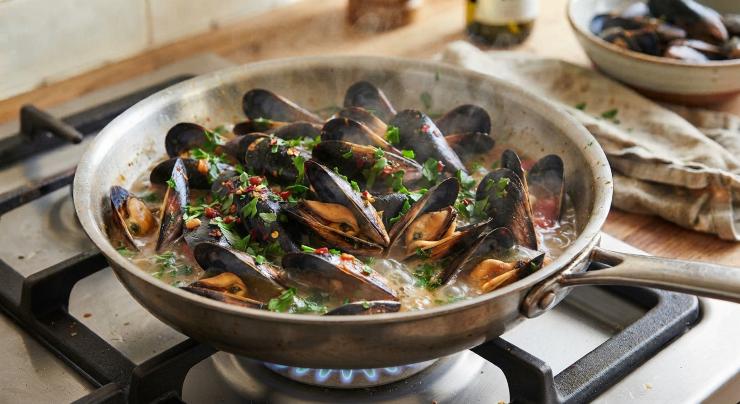 Per iniziare, pulite le cozze sotto l’acqua corrente fredda, eliminate eventuali impurità esterne raschiando i gusci con il dorso di un coltellino e tirate via la barbetta filamentosa con un movimento deciso. Scartate i molluschi con le valve rotte.Prendete un tegame capiente, versate un filo d’olio extravergine d’oliva e unite uno spicchio d’aglio. Aggiungete le cozze pulite, sfumate con il vino bianco secco, coprite con il coperchio e lasciate cuocere a fuoco vivace per circa 5 minuti, giusto il tempo di farle schiudere completamente.