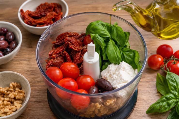 Cuocete la pasta in abbondante acqua salata, seguendo i tempi indicati sulla confezione per una cottura al dente. Nel frattempo, preparate il pesto: inserite nel mixer i pomodori secchi, 6 pomodorini, le olive, le noci, la ricotta, il basilico e l’olio extravergine d’oliva.