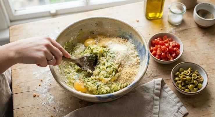 In una ciotola capiente, unite le zucchine ben asciutte alle uova, al parmigiano grattugiato e al pangrattato. Regolate di sale e pepe, quindi amalgamate il tutto fino a ottenere un impasto omogeneo. Tagliate i pomodorini a cubetti molto piccoli e tritate grossolanamente le olive verdi. Aggiungeteli all’impasto e lavorate ancora brevemente.
