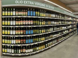 Scaffale con bottiglie di olio extravergine d'oliva al supermercato Ampio scaffale di un supermercato ben fornito con numerose marche e bottiglie di olio extravergine d'oliva in vetro scuro.